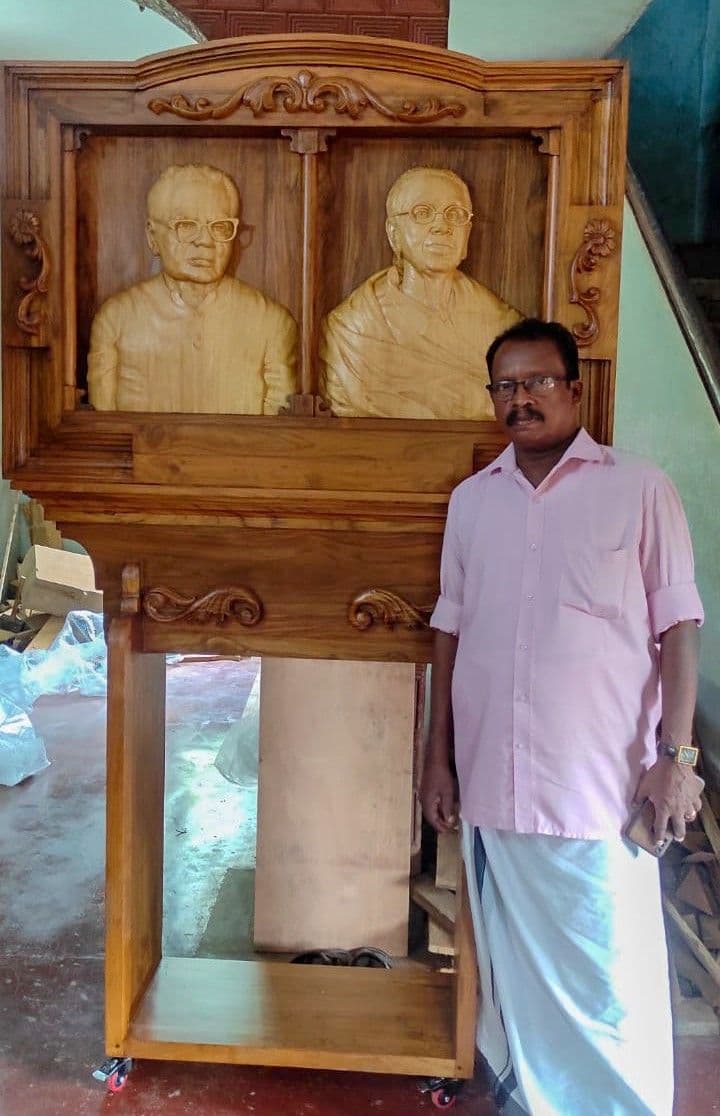 Master Artisan Shri Nagappan standing with a hand-carved teak memorial portrait relief shrine